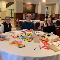 A group of women sitting at a table decorating lunch bags